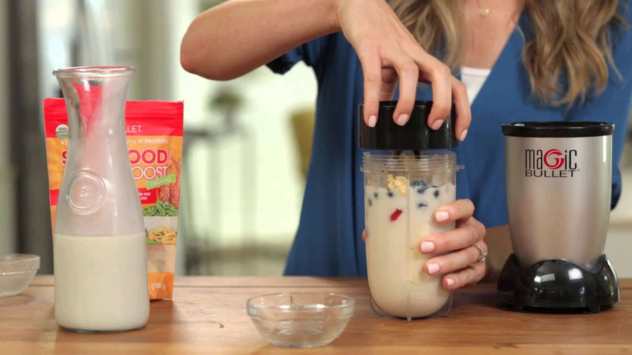 A pink berry and banana smoothie in the Magic Bullet cup next to fresh strawberries and blueberries