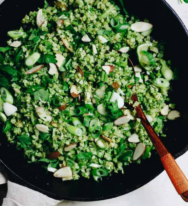 Paleo broccoli fried rice topped with scallions, cilantro and sliced almonds, with lime wedges
