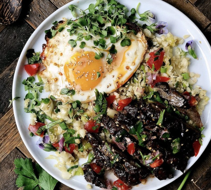 Sliced paleo Filipino skirt steak served over cauliflower fried rice with a fried egg and fresh tomato parsley sauce