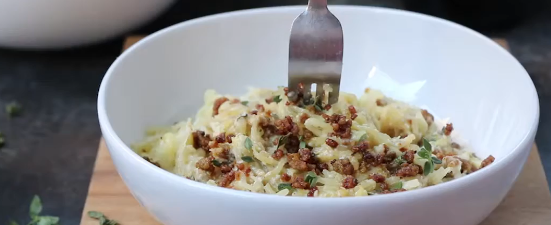 Paleo spaghetti squash noodles tossed in cashew cream sauce and topped with crispy minced pork crumbles in a white bowl