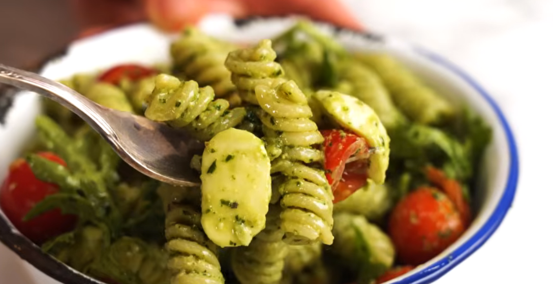 Bowl of broccoli pesto pasta salad with chickpea rotini, broccoli florets and halved grape tomatoes