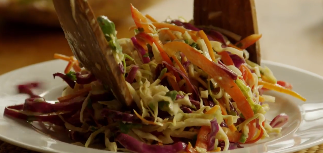 Bowl of paleo Asian coleslaw with shredded green and purple cabbage, bok choy, snow peas, carrots and scallions in sesame dressing