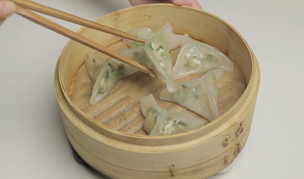 Homemade gluten-free dumpling wrappers cut into squares, with folded wontons floating in broth in a white bowl